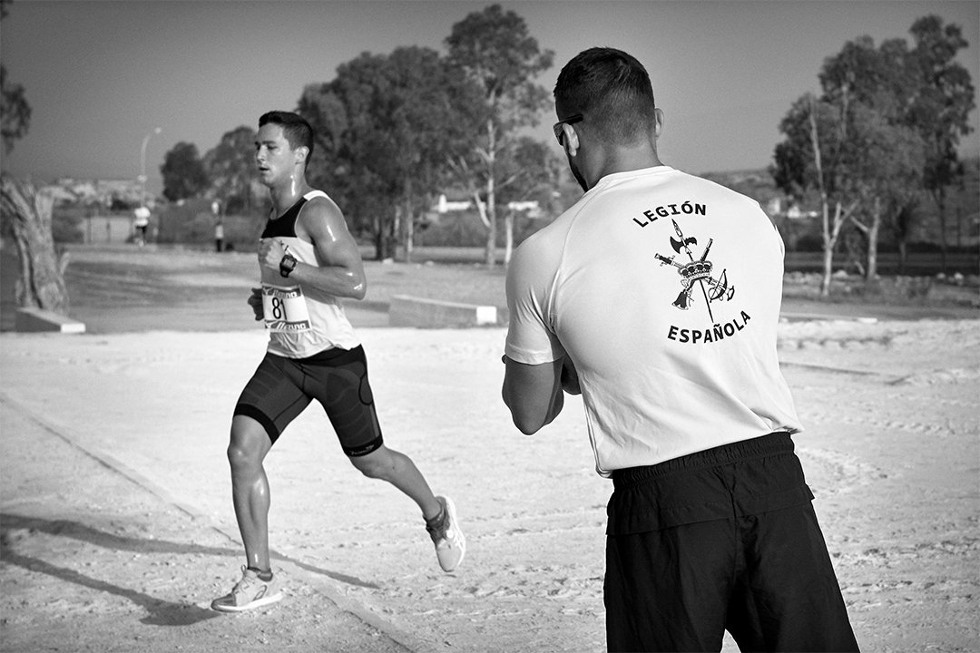 A runner passing a person wearing a Spanish Legion T-shirt.